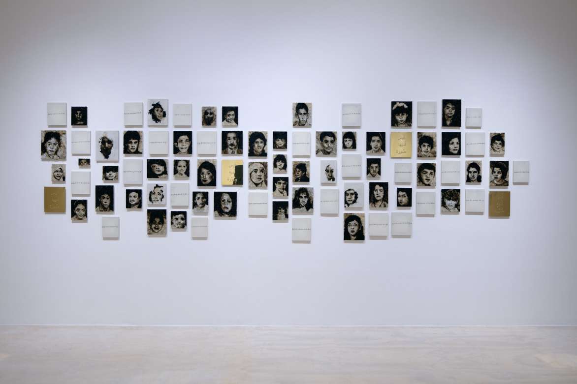 Installation view of a series of pictures and pieces of paper with text on wall.