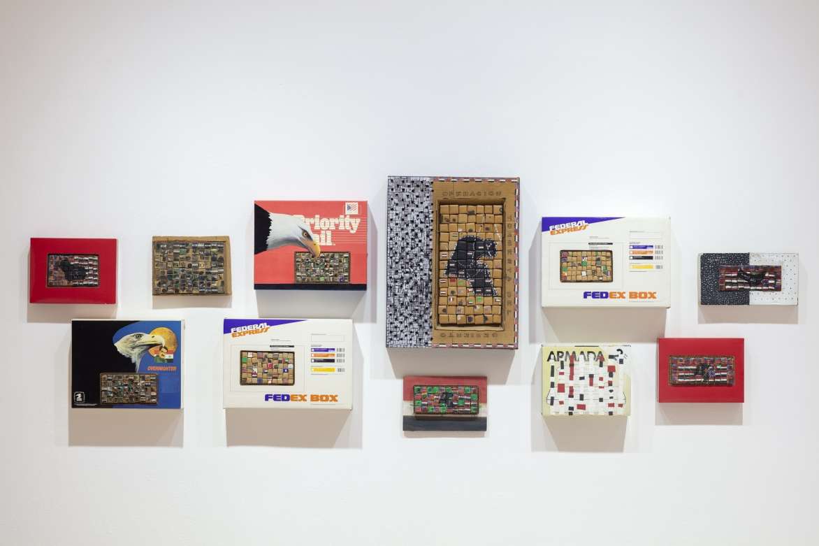 A series of small shipping boxes mounted to the wall. The boxes have been cut into forming grids of other small boxes.