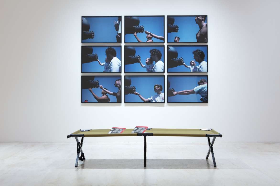 A grid of photographs of people in front of and touching a large piece of artillery. In front of the photographs is a table.