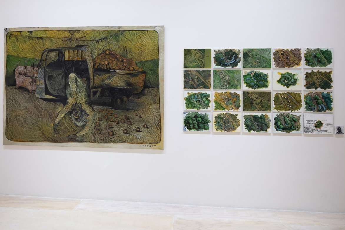 A wall with a large abstract painting on the left and a grid of smaller abstract paintings on the right.