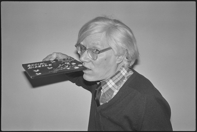 Andy Warhol pretending to bite into a chocolate bare with the words 