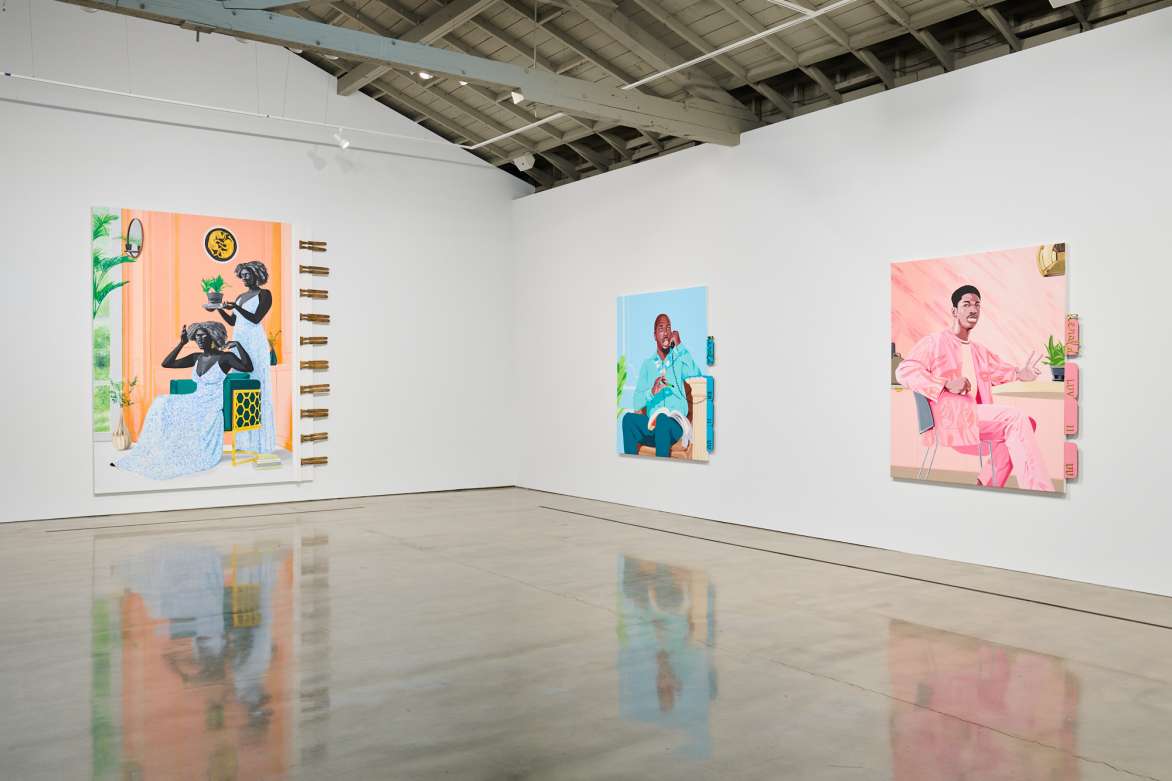 View of the back corner of a gallery with large colorful portraits on both walls.