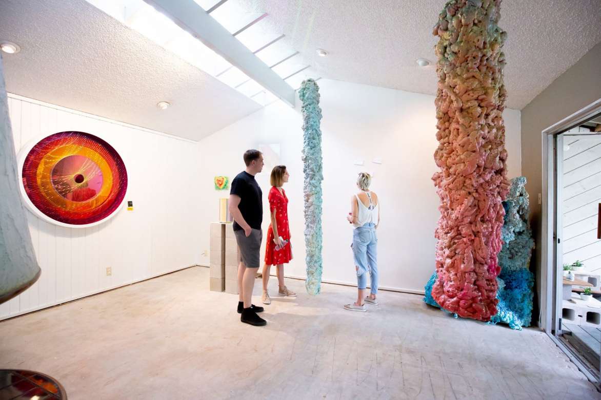 Three people standing in a gallery with two large sculptures.