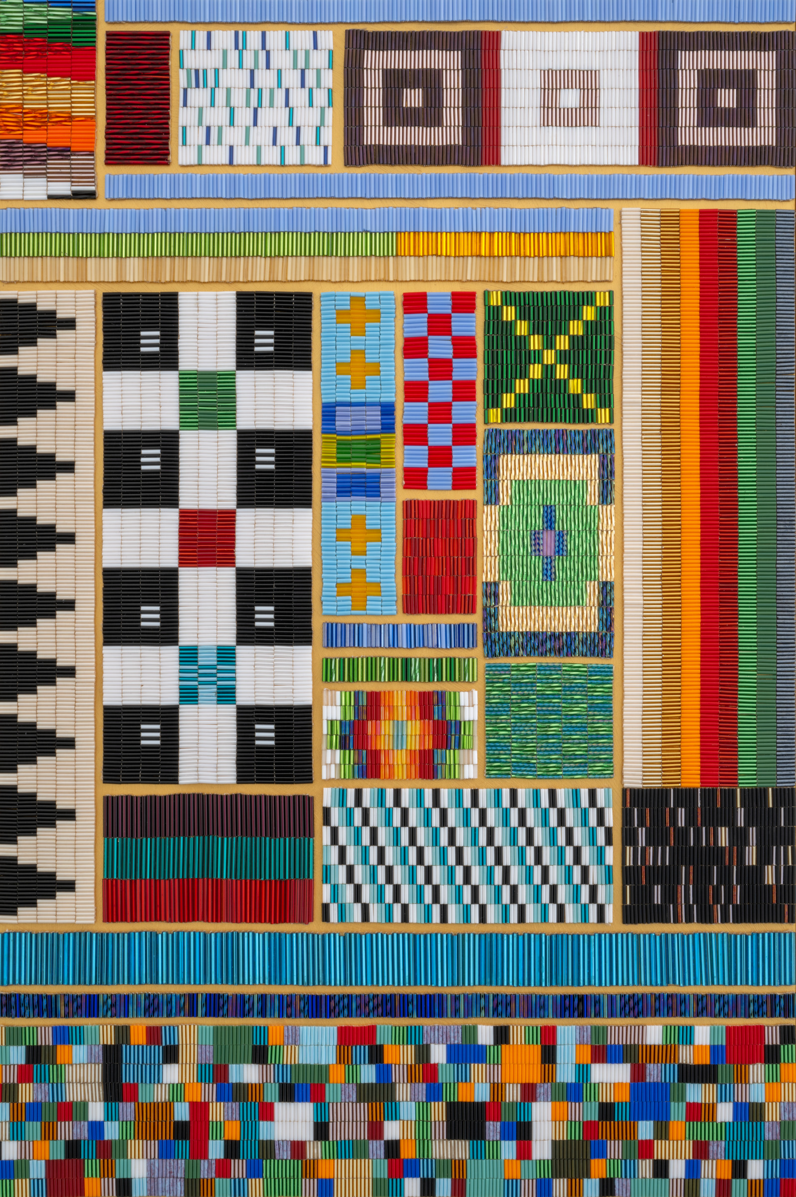 A close up on a patchwork of beaded panels. Each is sewn into different geometric patterns, many are highly reflective
