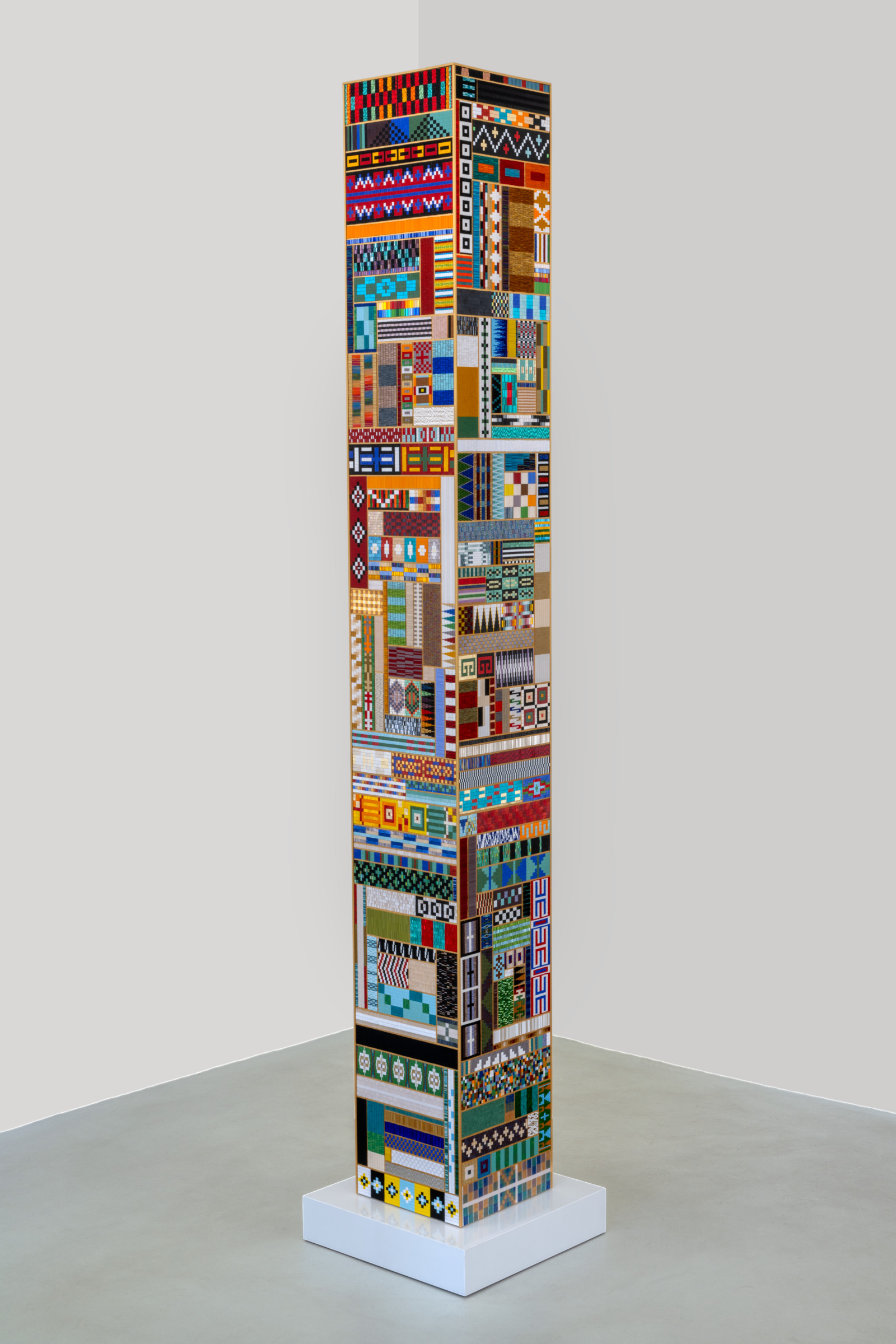 A large columnar sculpture made up of a patchwork of beaded panels. Each is sewn into different geometric patterns, many are highly reflective
